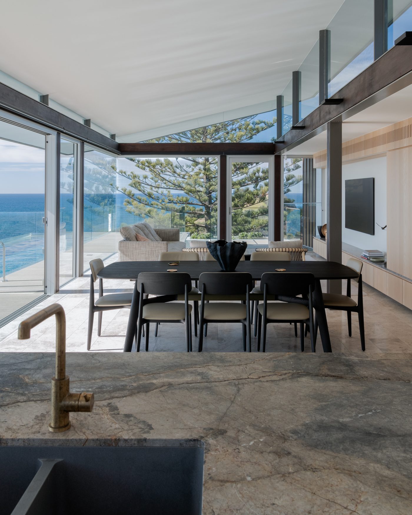 Marble benchtop with a brass tap and black sink, looking through to a dining table and the ocean at Terrigal