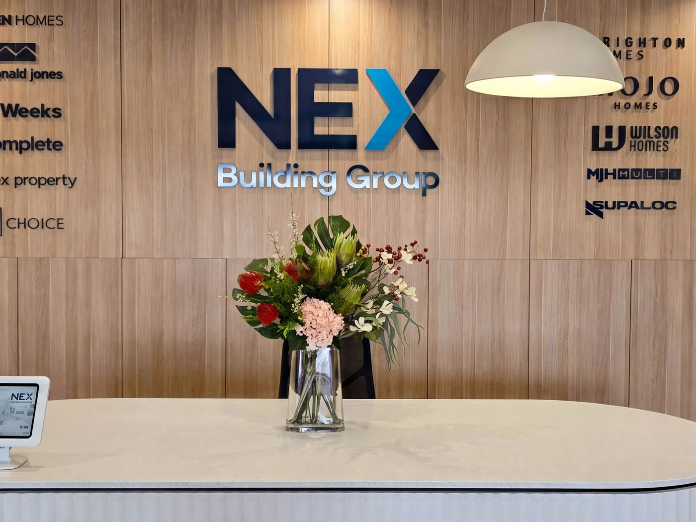 Curved white stone reception desk in front of a timber wall with the NEX Building Group sign