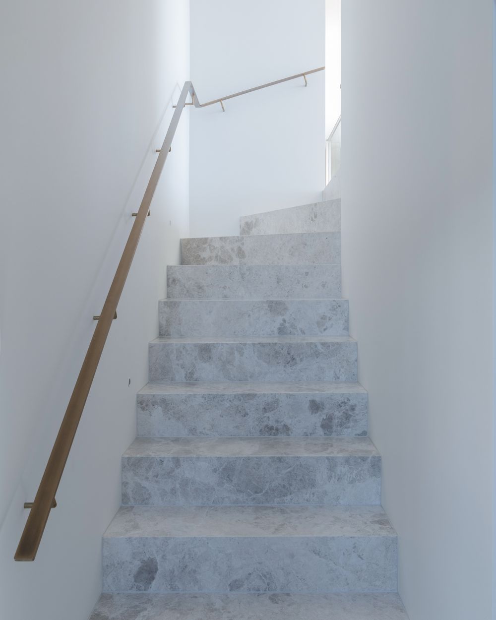 Marble stair treads with a brass handrail in a white stairwell at Terrigal